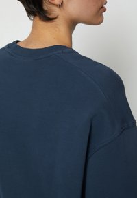 Sudadera azul marino con cuello redondo, puños acanalados y corte relajado. Textura suave, costuras visibles y hombros caídos.