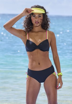 Schwarzes Bikini-Oberteil mit pinken Trägern, passender schwarzer Bikini-Unterteil mit Kordeln und neonfarbenen Akzenten, kombiniert mit einer gelben Visiermütze und einem Armband.