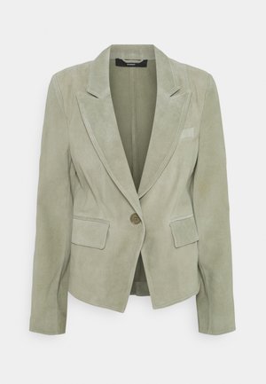 Blazer en suède vert clair avec manches longues, revers à crans, fermeture à un bouton et deux poches à rabat devant.