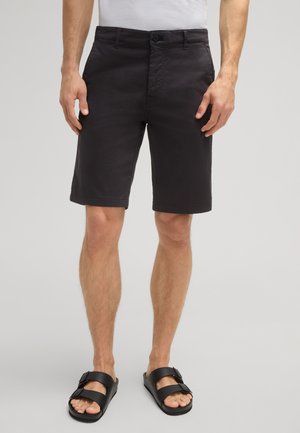 Shorts gris foncé en coton avec une texture lisse, dotés d'une fermeture bouton à l'avant et de poches latérales, portés avec des sandales à lanières noires.