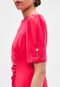 Fuchsijové šaty s krátkymi puff rukávmi, s kovovými gombíkmi na manžetách a zberanými detailmi na boku. Mäkká látka s hladkou textúrou.