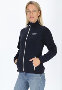 Marinblå fleecejacka med hög krage, fullständig dragkedja fram och kontrasterande vit dragkedja. Har två sidofickor med dragkedjor. Mjuk textur.