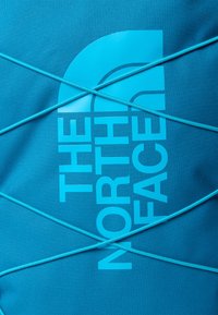 Kék szövet táska, amelyen vastag betűkkel szerepel "The North Face" logó, elöl pedig keresztbe fűzött gumiszalag minta.