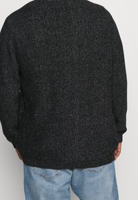 Svart stickad tröja med metalltrådar, rund halsringning och långa ärmar, parat med ljusblå jeans.