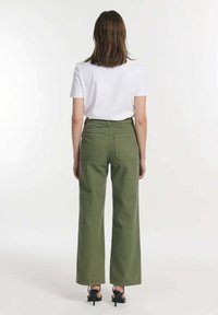 Groene brede broek met een hoge taille, voorzien van twee achterzakken en een knoopsluiting, gedragen met een effen witte T-shirt met korte mouwen.