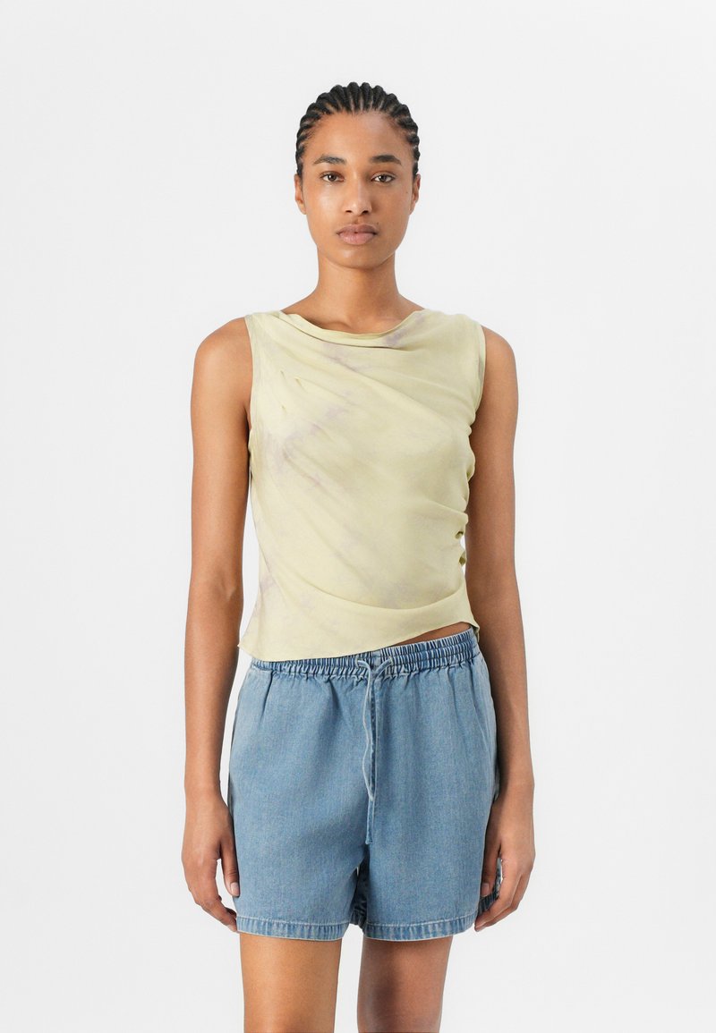 Light yellow sleeveless top with draped design and subtle irregular pattern, paired with blue denim shorts featuring an elastic waistband.