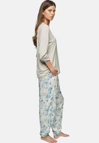 Haut gris clair à manches longues avec des manches retroussées, associé à un pantalon de pyjama floral beige ample avec des motifs bleus.