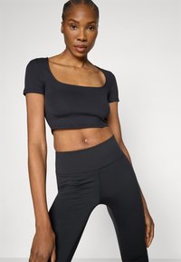 Čierne krátke tričko s krátkymi rukávmi a štvorcovým výstrihom, kombinované s čiernymi legínami s vysokým pásom. Hladká, elastická látka.