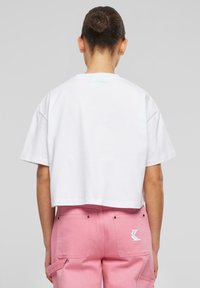Tricou scurt din bumbac alb, cu mâneci scurte, asortat cu pantaloni roz care au buzunare laterale de tip cargo și un detaliu cu logo alb pe spate.