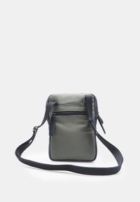 Zelená nylonová crossbody taška s čiernym koženým akcentom, obdĺžnikového tvaru, so zipsovým predným vreckom a nastaviteľným popruhom.