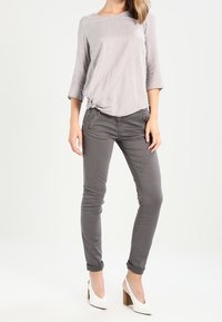 Grå stribet top med en knyttet detalje i siden, parret med grå slim-fit bukser og hvide hæle, der viser et afslappet outfitdesign.