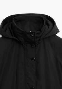 Veste noire à capuche avec un devant à boutons, tissu texturé et col montant. Le design présente un style simple et minimaliste.