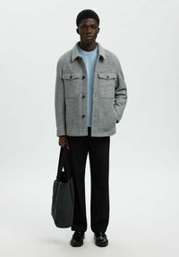 Sivi kaput od vune s mješavinom vlakana sa dva prednja džepa, nošen preko svijetloplavog pletenog pulovera, uparen s crnim širokim hlačama i tamnom torbom.