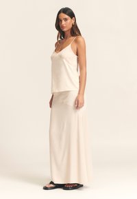 Siidist kampsun ja sobiv maksiseelik pehmes beežis. Omavad reguleeritavaid spagetitramme ja siledat tekstuuri, kantud mustade sandaalidega.