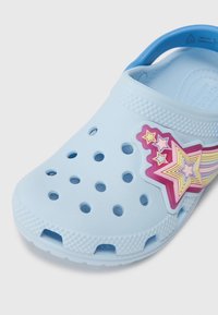Clogs en plastique bleu clair avec des trous de ventilation, arborant un design étoilé multicolore et une surface supérieure lisse et texturée.