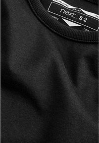 Schwarzes Baumwoll-T-Shirt mit runder Ausschnittkante und geripptem Rand. Das Etikett trägt die Aufschrift "next. 82," an der Kragenpartie angebracht. Glatte Textur.