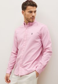 Camicia button-down rosa in tessuto di cotone con vestibilità slim. Caratterizzata da colletto, maniche lunghe e un piccolo logo nero sul petto.