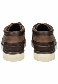 Botas de tobillo de cuero marrón y lona con un acabado texturizado, suela de goma blanca y la marca "TOMS" en el talón. Acentos de costura doble.