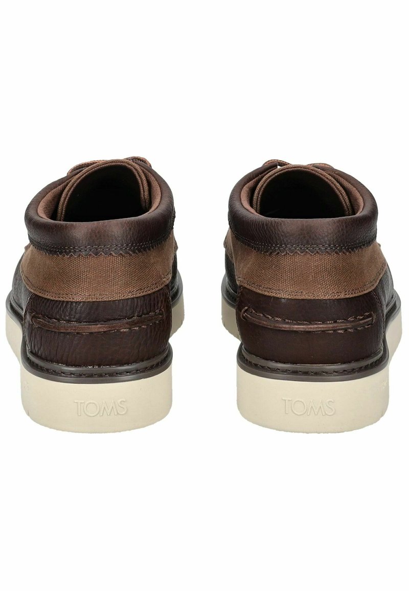 Botas de tobillo de cuero marrón y lona con un acabado texturizado, suela de goma blanca y la marca "TOMS" en el talón. Acentos de costura doble.