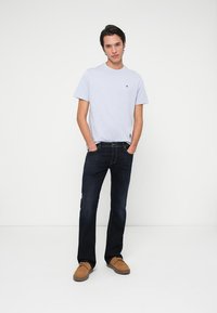 Svijetloplava majica s okruglim izrezom, tamne traperice i bež nubuk cipele. Jednostavan dizajn, bez uzoraka, s izvezenim logotipom na majici.