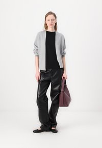 Šedý pletený cardigan přes černý top, doplněný černými koženými kalhotami a plochými černými botami. Drží burgundskou kabelku.