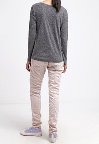 Světle šedá košile s dlouhým rukávem, růžové slim fit kalhoty s prošíváním a bílé tenisky s iridescentními akcenty; jednoduché pozadí.