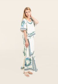 Weißes Stoffoutfit mit blauen und grünen Blumenmustern, kurzen Ärmeln und einem geschichteten Rock. Abgerundet mit einer passenden Tasche und Riemchensandalen.