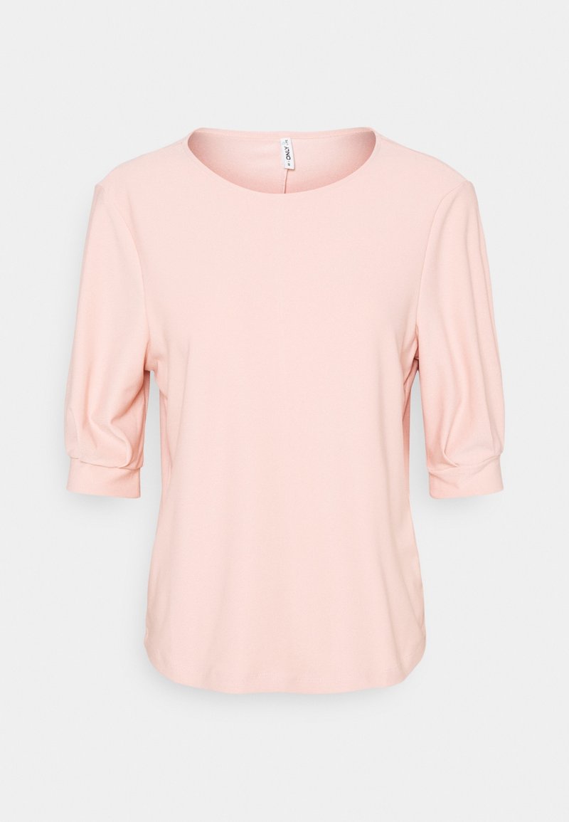Blouse rose clair pour femme avec encolure ronde et manches bouffantes trois-quarts sur un fond uni.