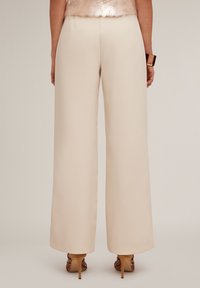 Beige wijde broek van zachte stof met een getailleerde pasvorm. Voorzien van een strakke ontwerp, voor plooien en een zijrits sluiting.