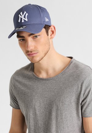 Navyblaues Cap mit weißem New York Yankees Logo, gebogenem Schirm und verstellbarem Riemen. Graues T-Shirt mit Rundhalsausschnitt und kurzen Ärmeln.