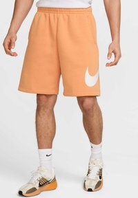 Pantalones cortos de sudor naranja con cintura elástica y gran logo blanco de Nike en el muslo izquierdo. Presenta bolsillos laterales y una textura de tela suave.