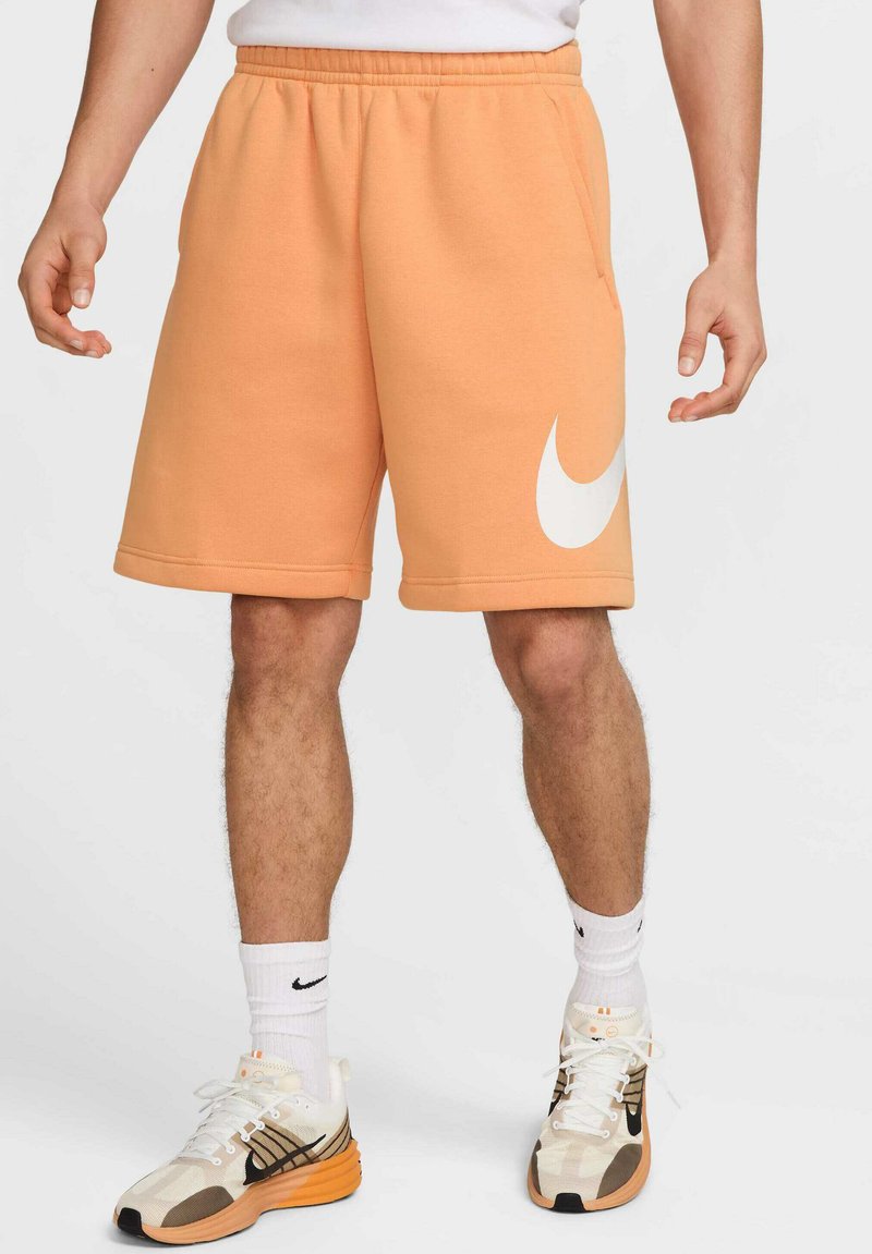 Pantalones cortos de sudor naranja con cintura elástica y gran logo blanco de Nike en el muslo izquierdo. Presenta bolsillos laterales y una textura de tela suave.