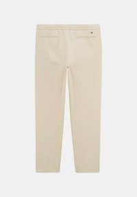 Pantalons couleur crème avec une taille élastique, deux poches arrière et une texture lisse, sans motifs visibles ni accents matériels.