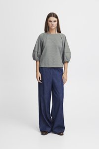 Haut gris à motifs avec des manches ballon associé à un jean bleu foncé à jambes larges. Tissu lisse avec des imprimés géométriques en losanges.