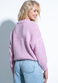 Różowy dziany sweter o luźnym kroju, z prążkowanym kołnierzem i długimi rękawami, noszony z jasnoniebieskimi spodniami z wysokim stanem.