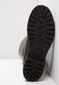 Črne usnjene podplate čevljev z globokim vzorcem; označene z velikostjo 37 in okrožnim logotipom; zaobljena oblika in gladka tekstura.