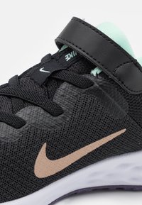 Sapatilha atlética preta com tecido em malha, detalhes em verde-menta e logótipo da Nike em bege. Apresenta um colar acolchoado e uma sola flexível.