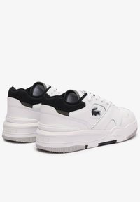 Zapatillas deportivas blancas con parte superior de cuero texturizado, cuello acolchado y un acento de malla negra en el talón. Detalle del logo en el lateral.