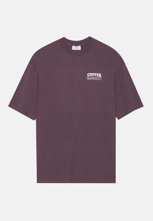 T-Shirt mit kurzen Ärmeln aus dunkelmauricefarbener Baumwolle. Mit einem weißen "COFFEE HARMONY" Grafik auf der Brust. Rundhalsausschnitt, lockere Passform, standardmäßiger Saum.