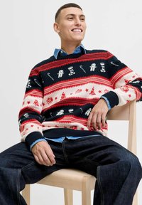 Suéter de punto en azul marino con patrones festivos en rojo y blanco, que incluyen muñecos de nieve y estrellas, combinado con una camisa de mezclilla, usado con jeans oscuros.
