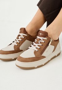 Brune og beige sneakers med en kombination af ruskind og læder, der har snørelukning, sidelukning med lynlås og tykke gummisåler.