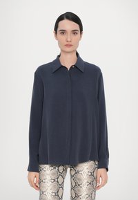 Camisa de manga larga azul marino con cuello y cierres de botón, combinada con leggings texturizados de piel de serpiente con patrones. Acabado de tela suave.