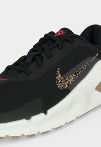 Μαύρο αθλητικό παπούτσι Nike με υφή σε καφέ και μαύρο μοτίβο στα πλαϊνά, κόκκινο λογότυπο στη γλώσσα και την μύτη, λευκή σόλα με καφέ λεπτομέρειες.