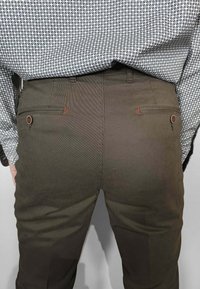 Pantaloni verde oliva con una trama liscia, caratterizzati da due tasche posteriori con chiusure a bottone e dettagli di cucitura contrastanti in rosso.