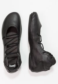 Paire de chaussures en cuir noir à lacets, bouts arrondis et semelles souples, vues de dessus et de côté sur fond blanc.