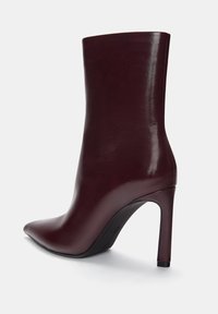 Burgunderfarbene Leder-Stiefelette mit spitz zulaufender Zehenpartie, glänzender Oberfläche, schlankem hohen Absatz und glatter Textur. Verfügt über ein elegantes, minimalistisches Design.