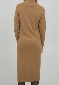 Vestido de punto acanalado color camel con cuello alto y mangas largas, que presenta una silueta ajustada y longitud hasta la mitad de la pantorrilla.