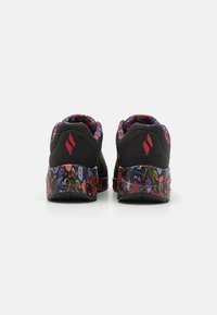 Chaussures de sport noires avec une semelle et un intérieur à motifs floraux colorés. Logo rouge à l'arrière. Forme arrondie avec col rembourré.