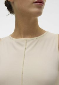 Beżowa bezrękawnik z okrągłym dekoltem, z subtelną teksturą prążkowaną i centralnym szwem. Gładkie wykończenie materiału.