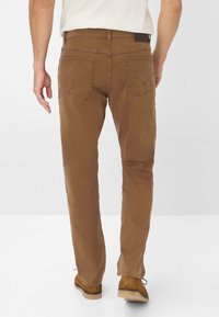 Pantaloni in cotone marrone con un design a gamba dritta, dotati di due tasche posteriori e cuciture decorative, abbinati a scarpe in suede marroni.